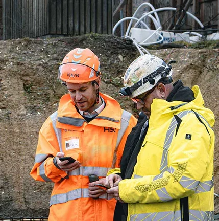 Zwei Bauarbeiter lesen auf der Baustelle Messwerte an einem mobilen Gerät ab
