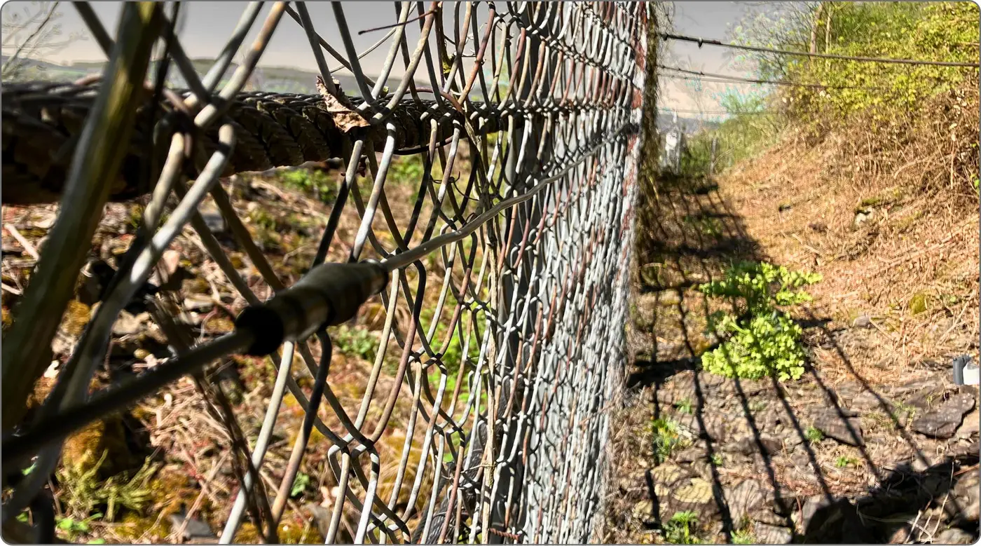 Drahtseilnetz einer Hangsicherung mit Sensorleitung, dahinter die Böschung