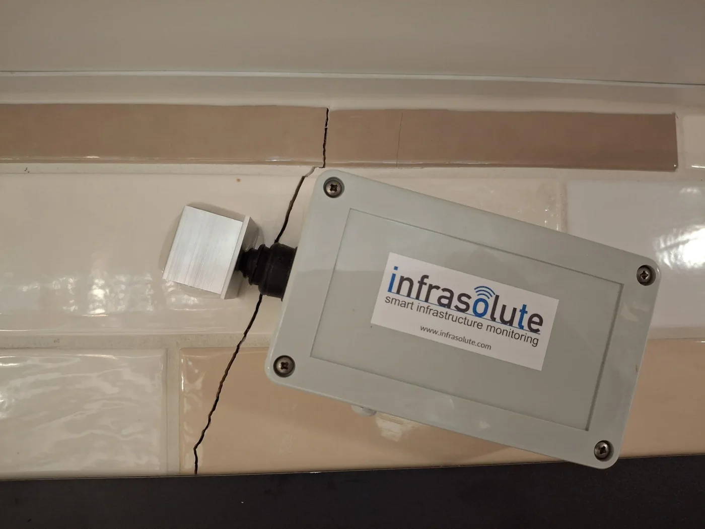 Risssensor an einer gefliesten Wand, der Riss verläuft durch die Fliesen