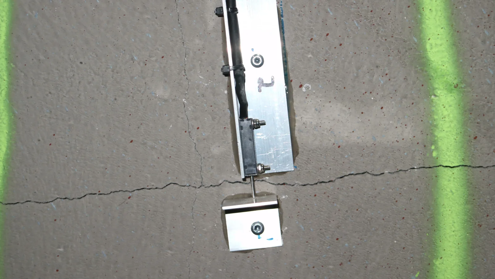Wegaufnehmer des Risssensors über einem Riss in einer Betonwand, mit Halterung auf beiden Rissseiten