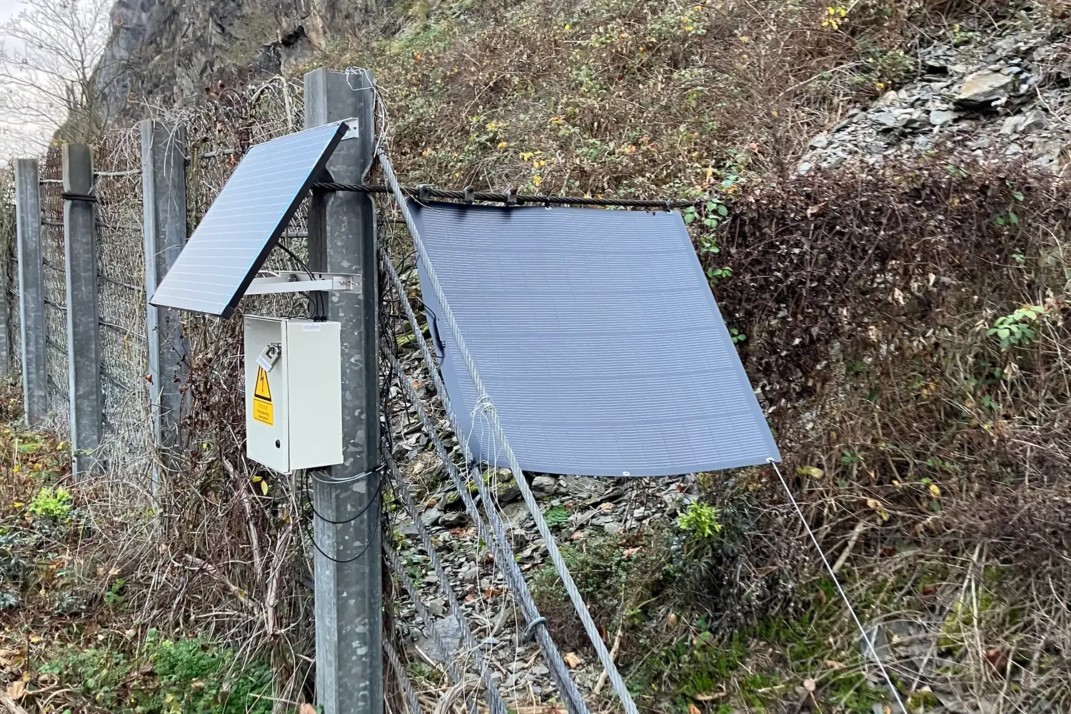 Gateway-Gehäuse mit zwei Solarpanels am Zaunpfosten der Hangsicherung