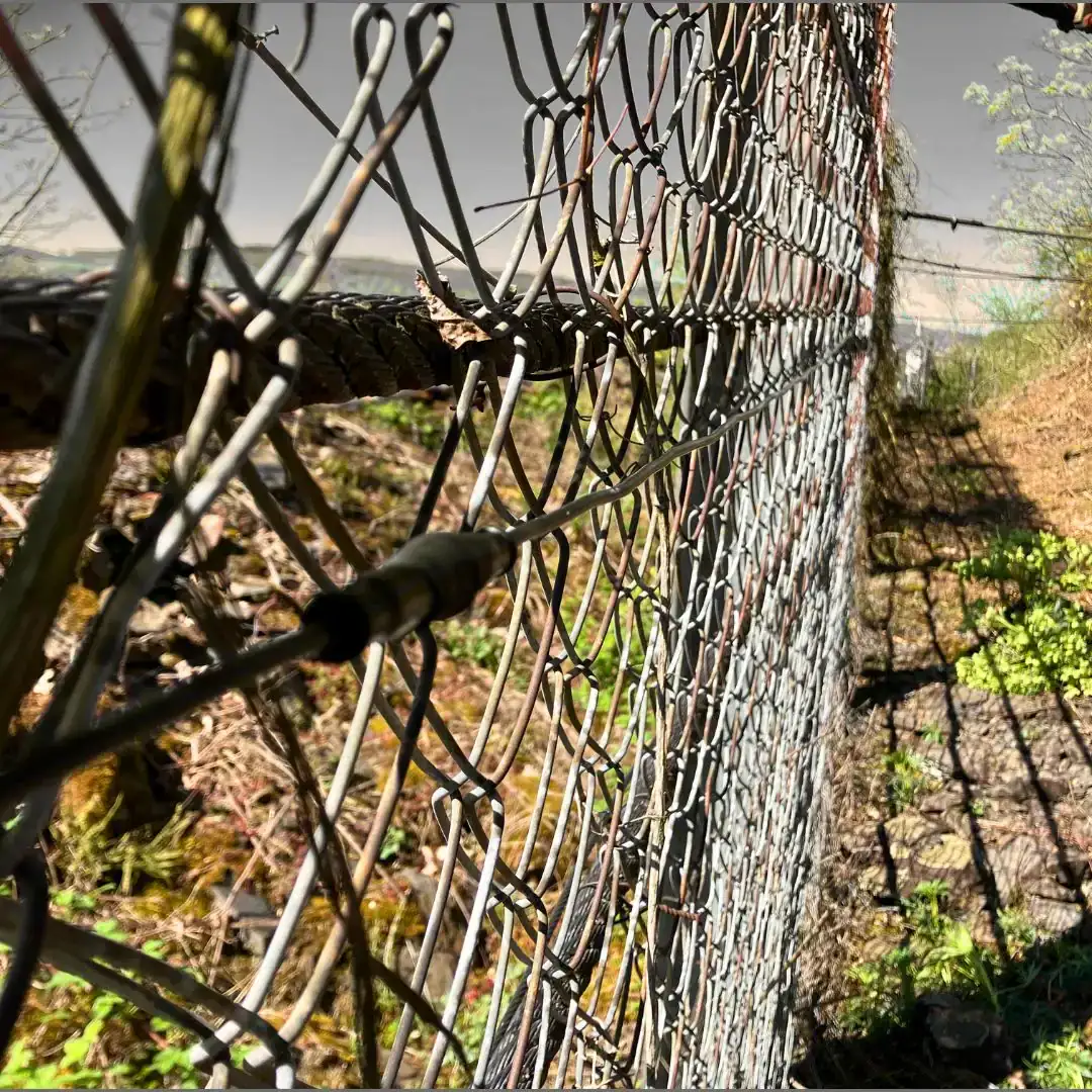 Drahtgeflecht eines Auffangzauns am Hang, im Netz eine dunkle Sensorleitung
